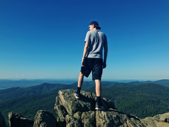 A young man looking out over the mountains while on a hike.